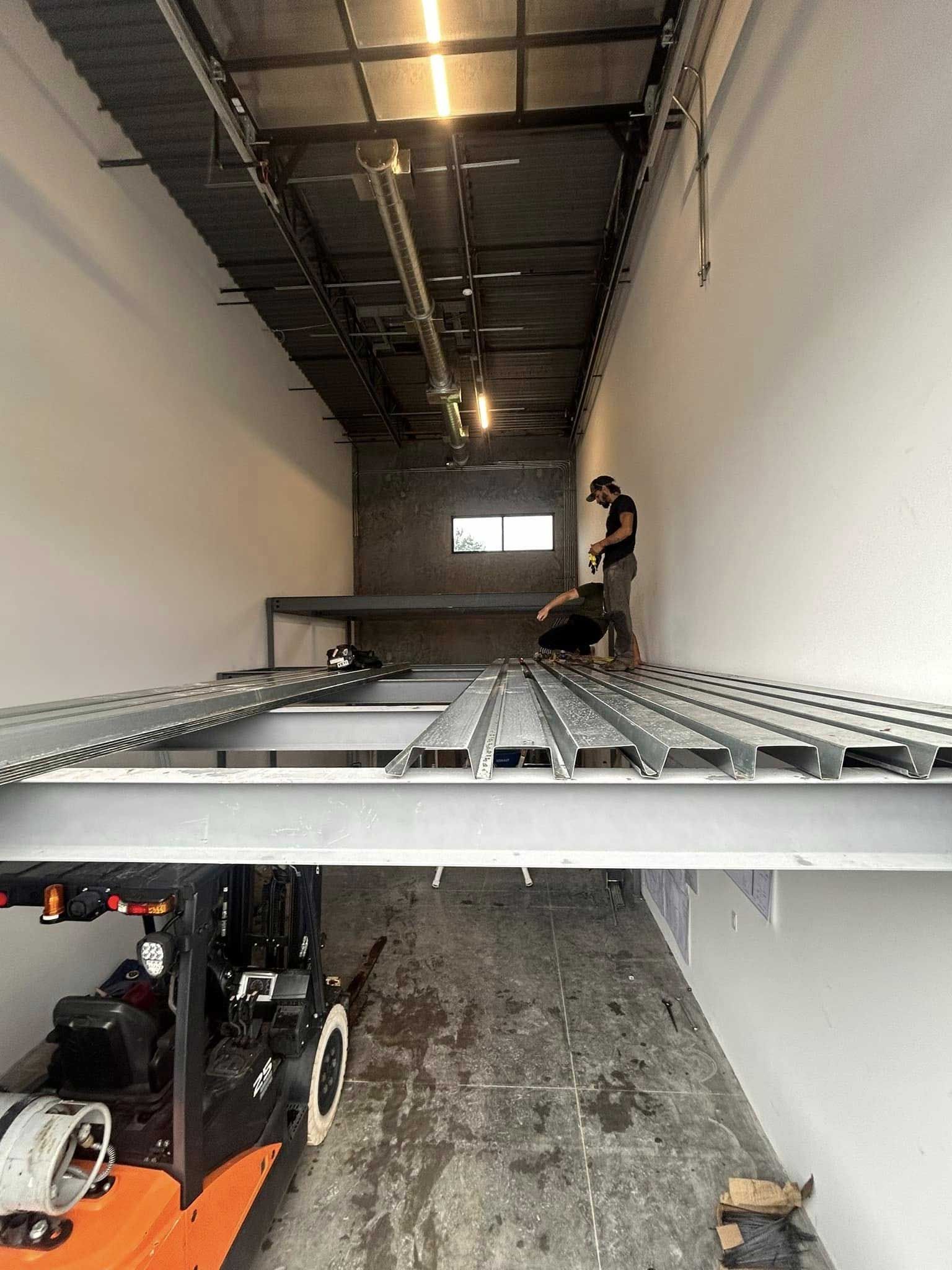 Inside a box truck, a worker secures equipment on metal rails under bright overhead lights.