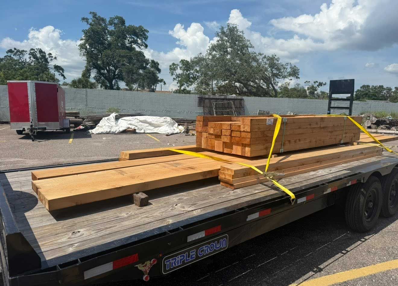 Lumber strapped on a flatbed trailer in a parking lot under a partly cloudy sky.
