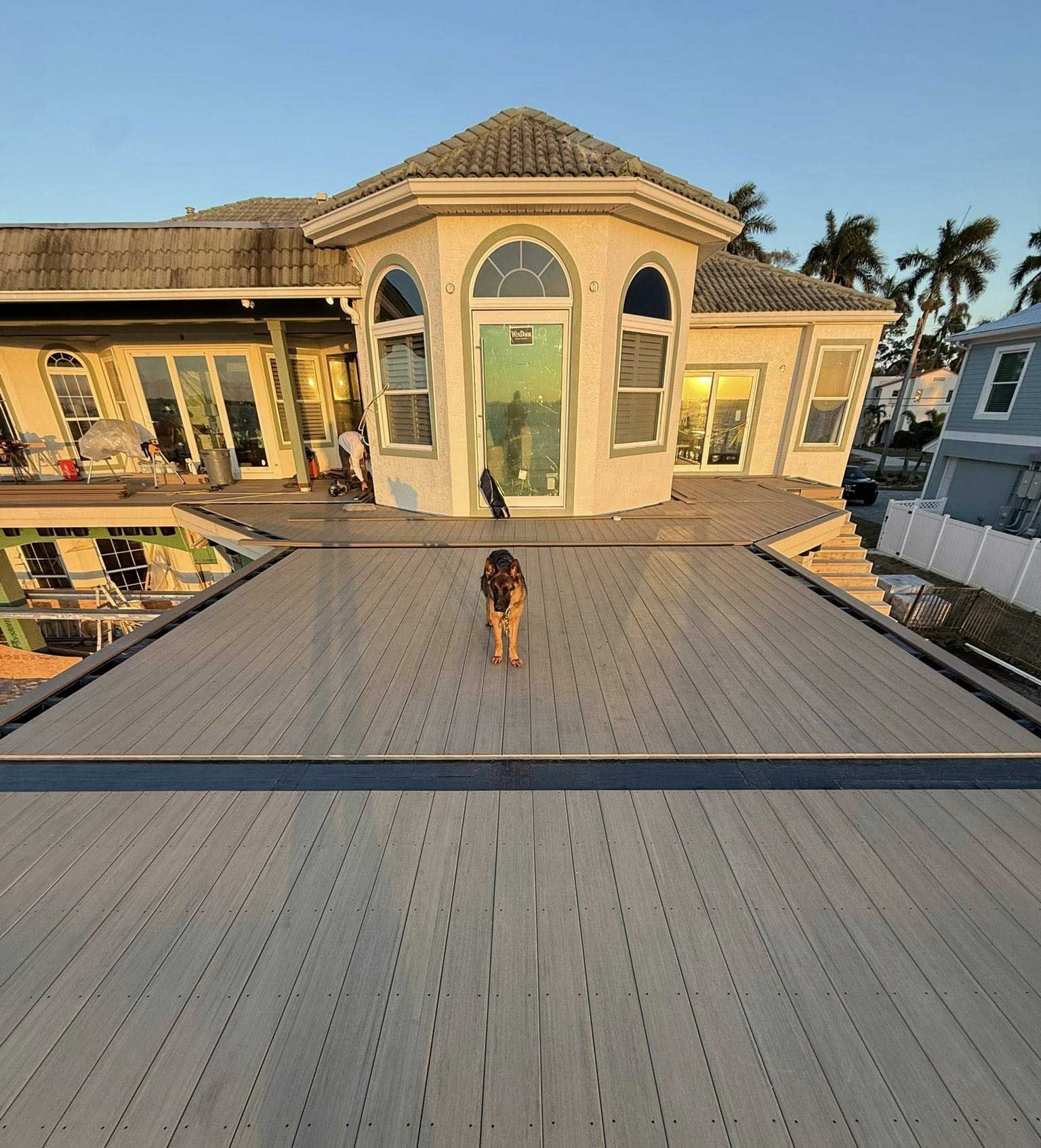 Large rooftop deck at sunset with a person standing in front of a beige house with arched windows.