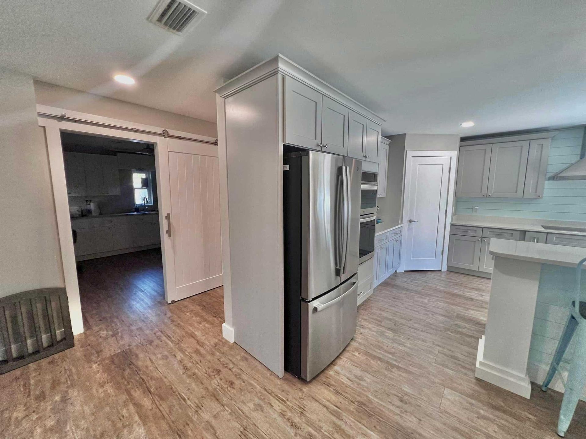 Modern kitchen with stainless steel fridge, white cabinets, and a doorway to a dark adjacent room