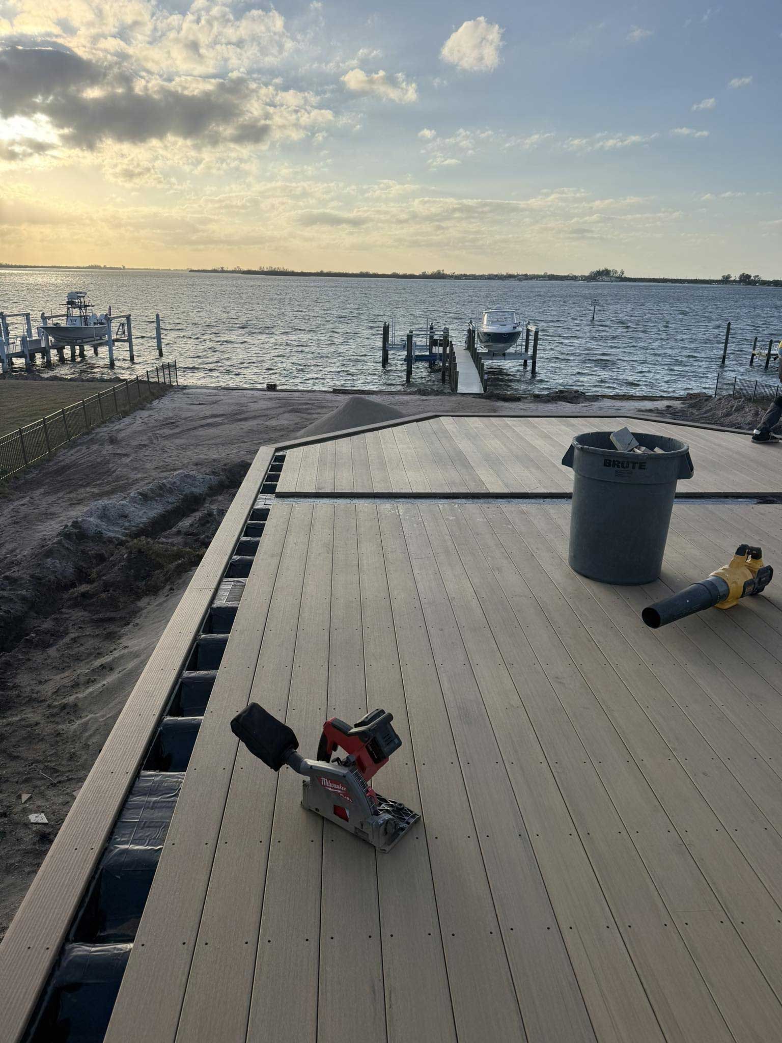 Dock at sunset by a calm lake, with chairs, a trash bin, and gear on a wooden deck.