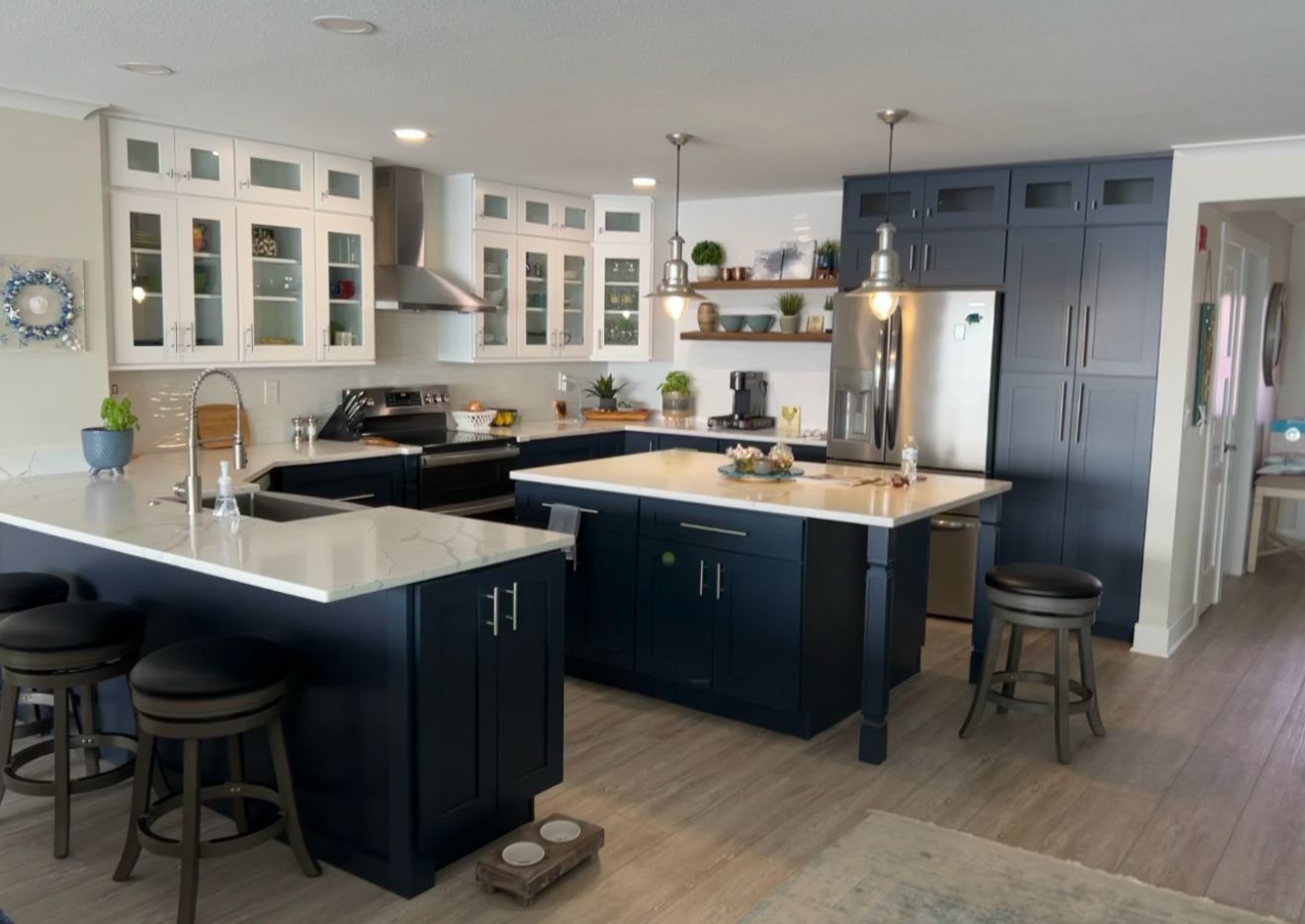 Modern kitchen with dark blue islands, white cabinets, stainless steel appliances, and stools on hardwood floor.