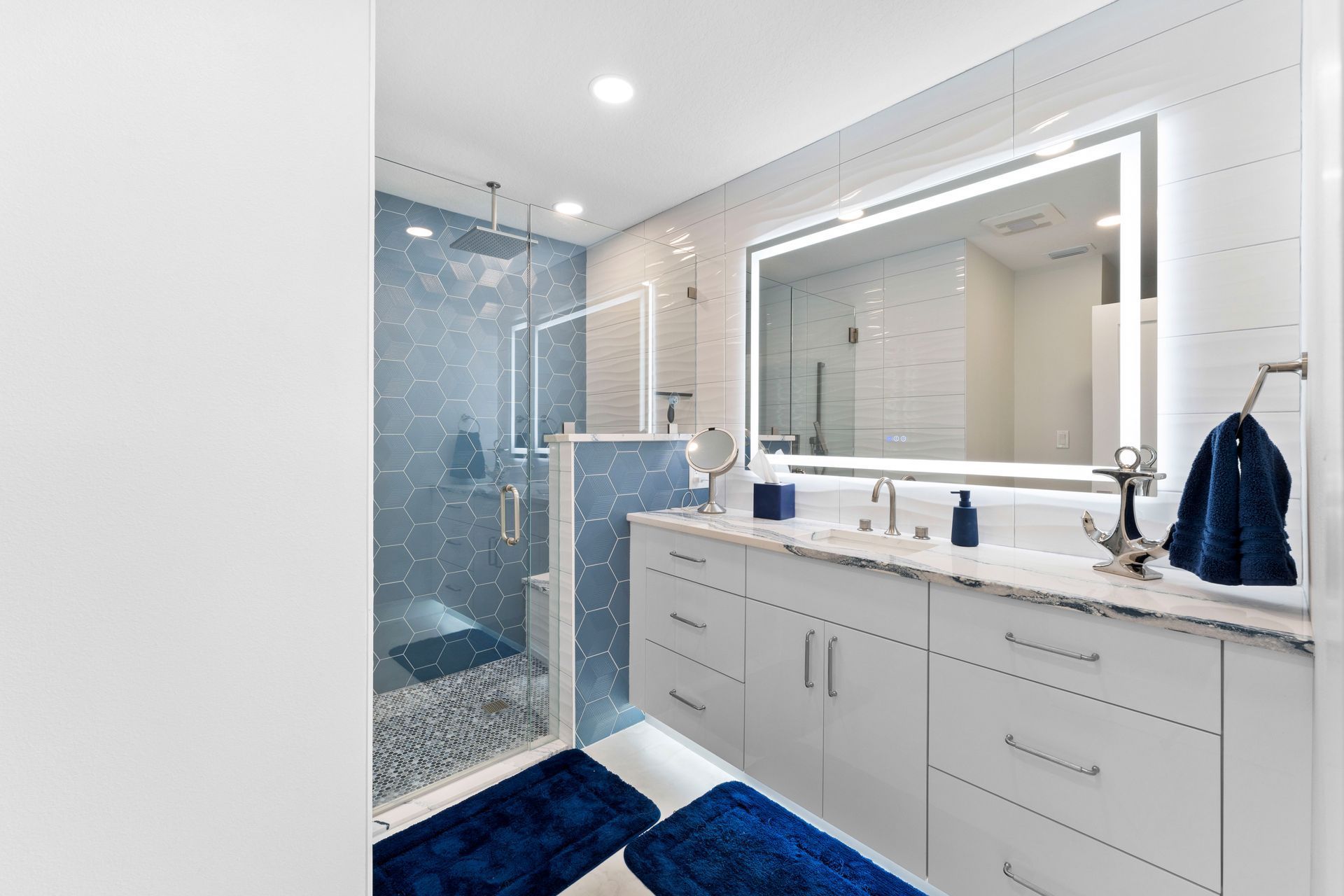 Modern white bathroom with double vanity, glass shower, large mirror, and blue accents.