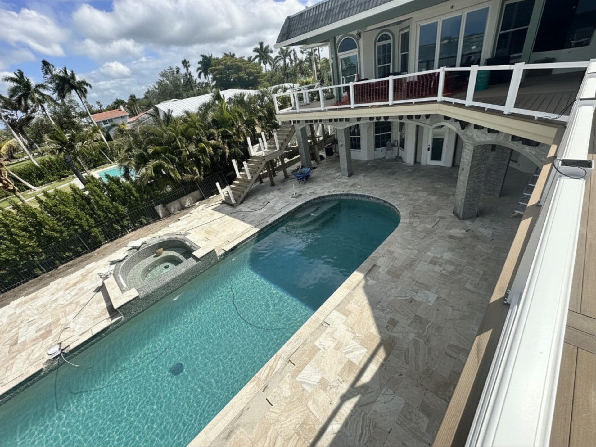 Modern house with a long blue pool and spa, viewed from an upper balcony in a sunny tropical setting.