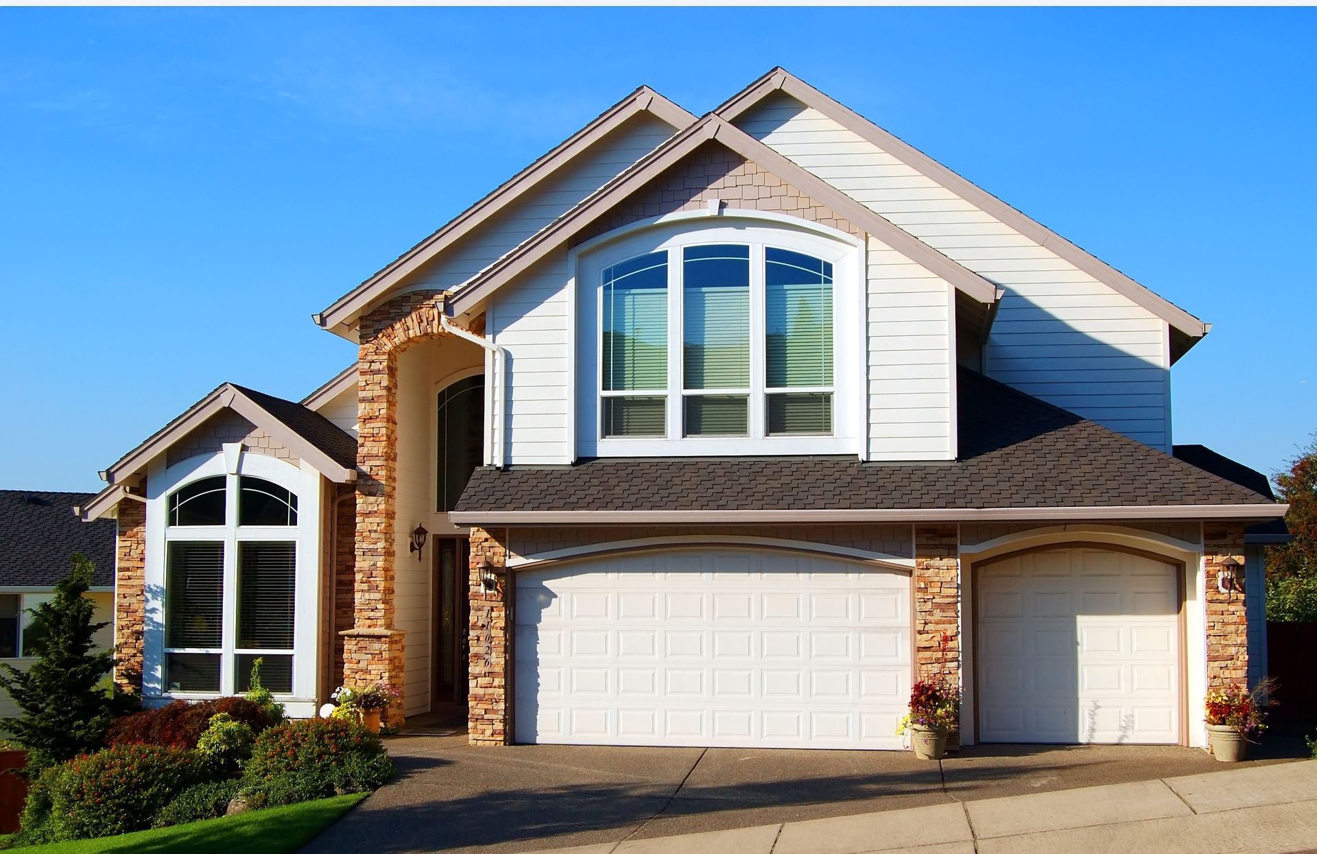 Suburban two-story house with white siding, brick accents, and a two-car garage under a blue sky