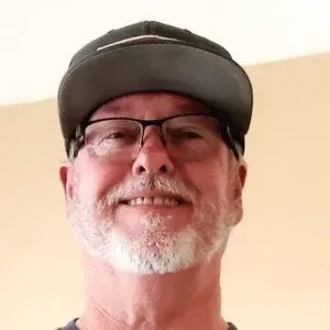 A man with a beard and glasses is wearing a hat and smiling.