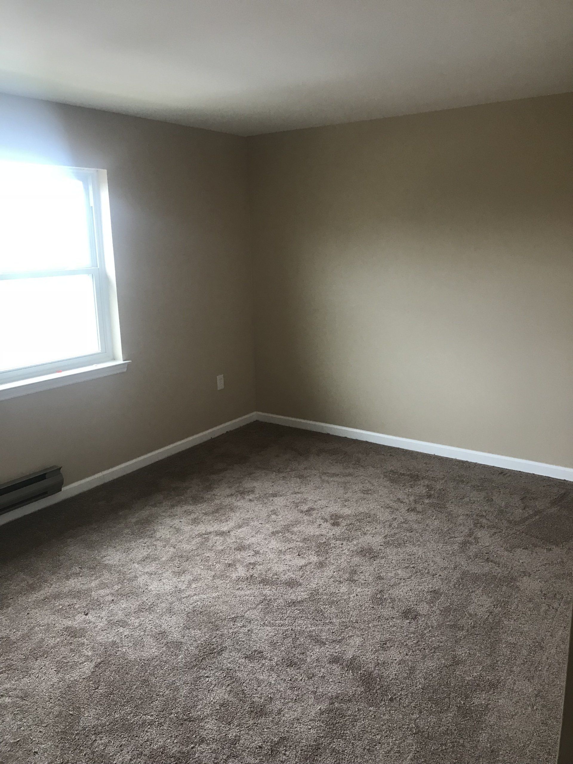 an empty room with a window and brown carpet