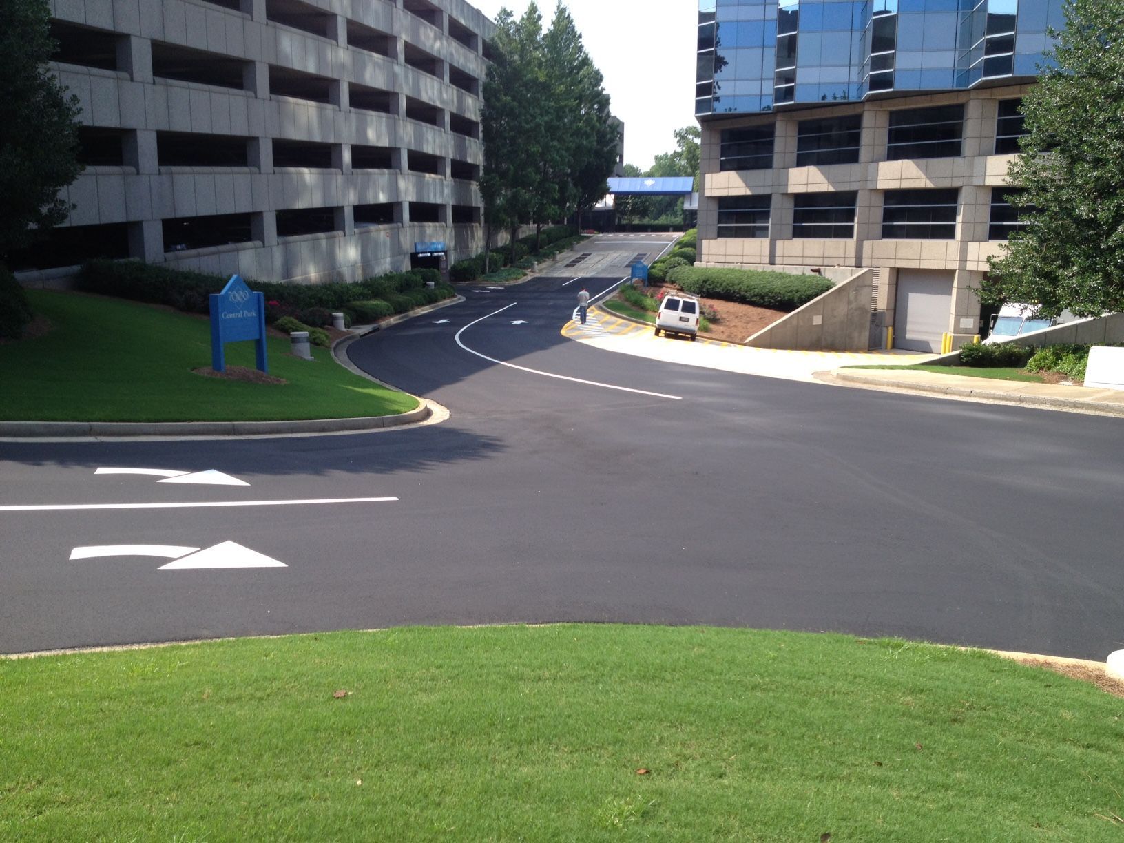 Paved road curves between two buildings. Green grass borders the road and surrounding area. Blue sky.
