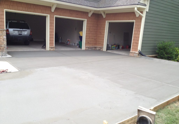 A freshly poured concrete driveway in front of a three-car garage with open doors. A vehicle is parked inside one bay.