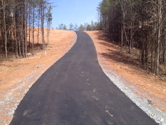 A newly paved asphalt road curves uphill through a clearing bordered by trees on both sides.