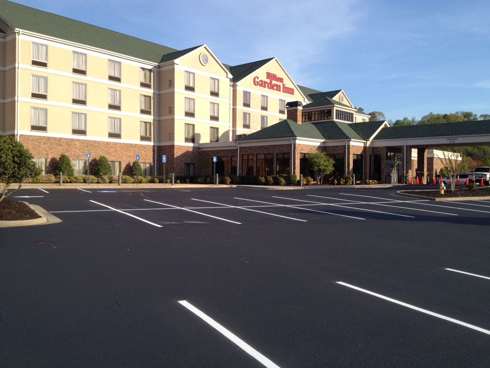 Hilton Garden Inn exterior with a freshly paved parking lot. The building is beige with a green roof.