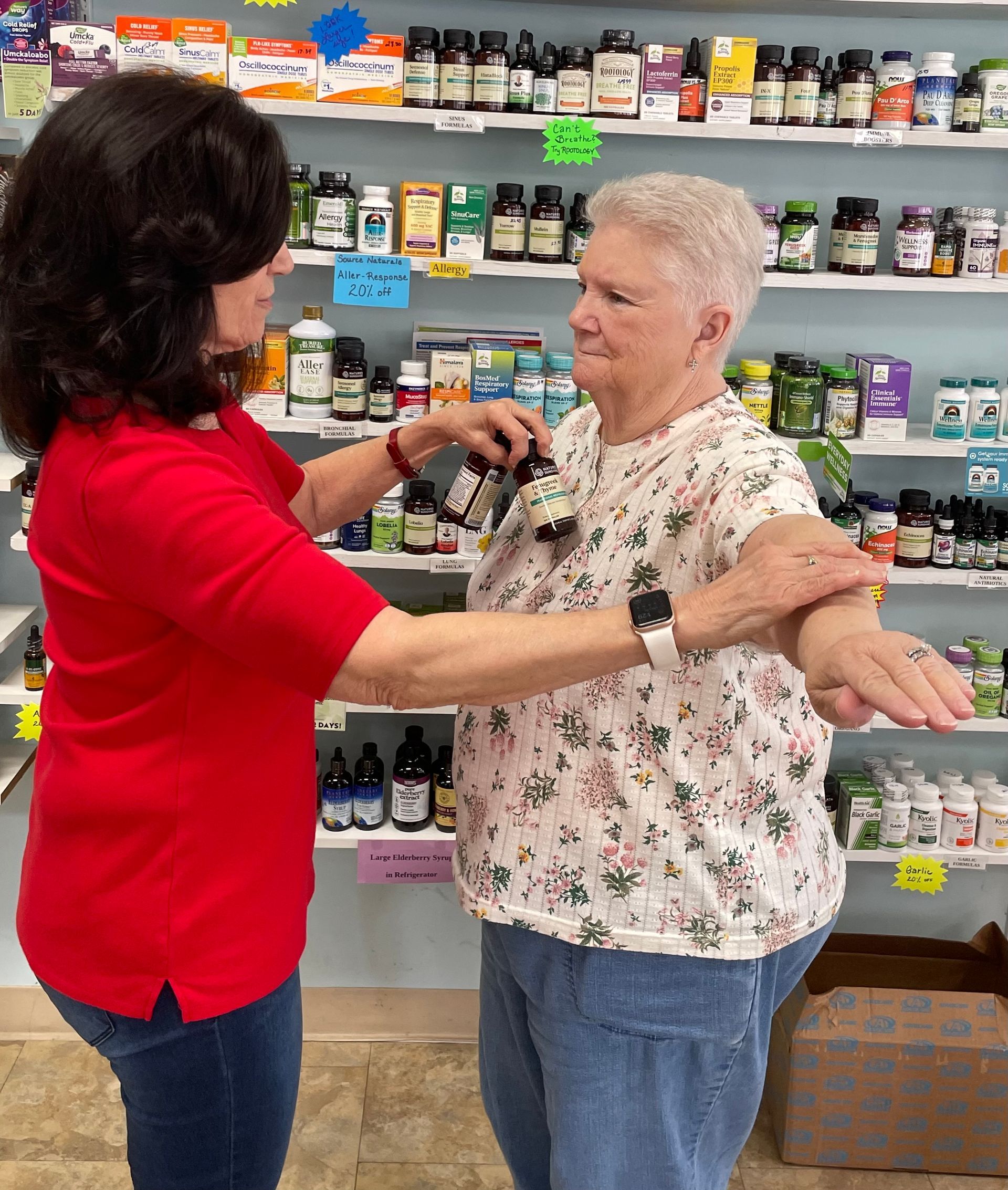 A woman is helping an older woman stretch her arms in a pharmacy.