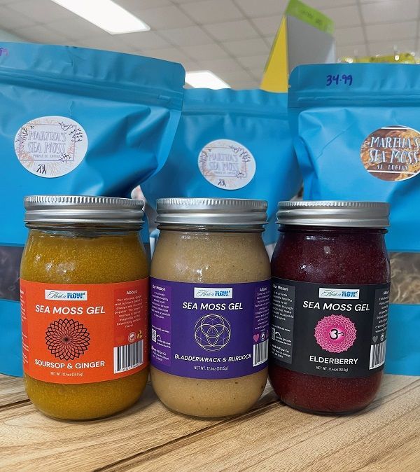 Three jars of different flavors of sea moss gel are sitting on a wooden table.