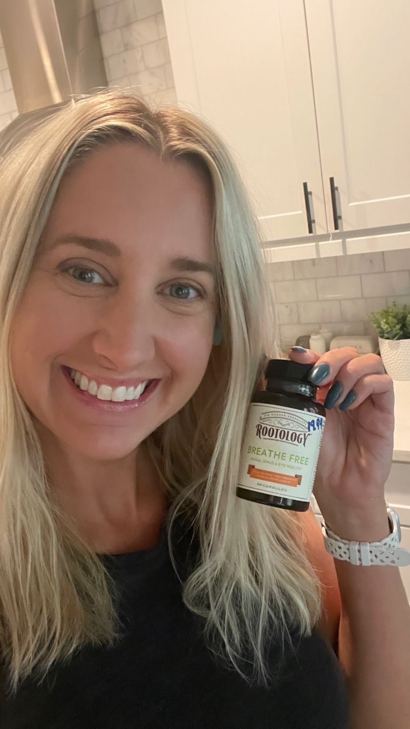 A woman is smiling while holding a bottle of vitamins.