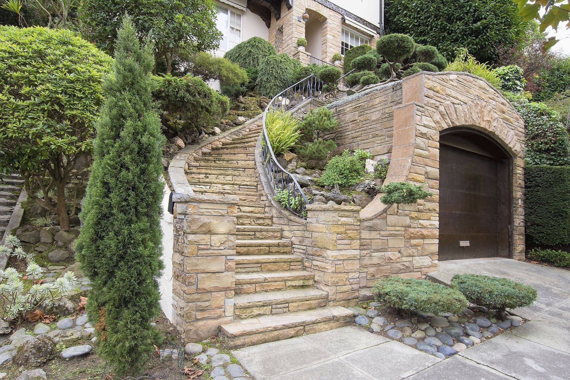 Stone steps leading to a garage entrance, surrounded by lush green shrubs and trees.