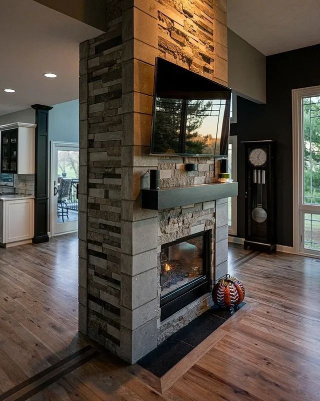 Fireplace with stone facade, TV, and black mantle, between living areas, with wood floors.