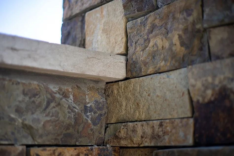 Close-up of stone wall corner with a light-colored ledge. Stone colors vary from tan to dark brown.