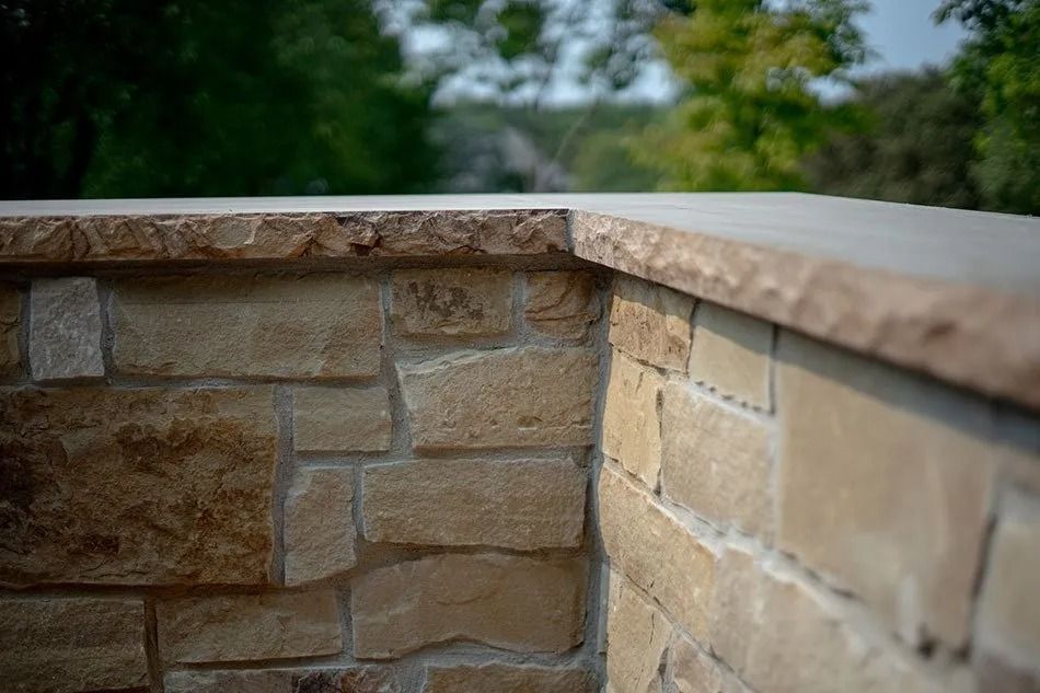 Stone wall with a smooth top, outdoors with blurred green trees in the background.