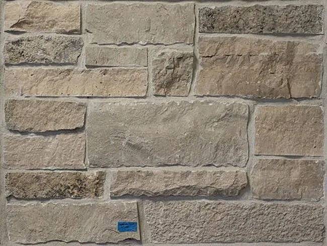 Rough-hewn stone wall in shades of beige and gray, with visible mortar between the rectangular and irregularly-shaped stones.