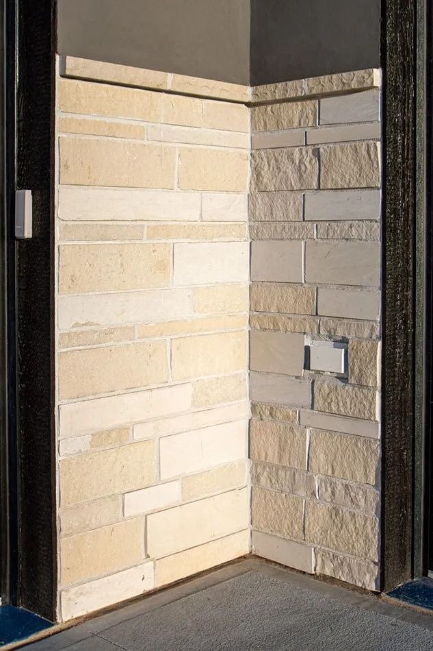 Corner of building with tan stone facade; light tan top, dark frame on sides.