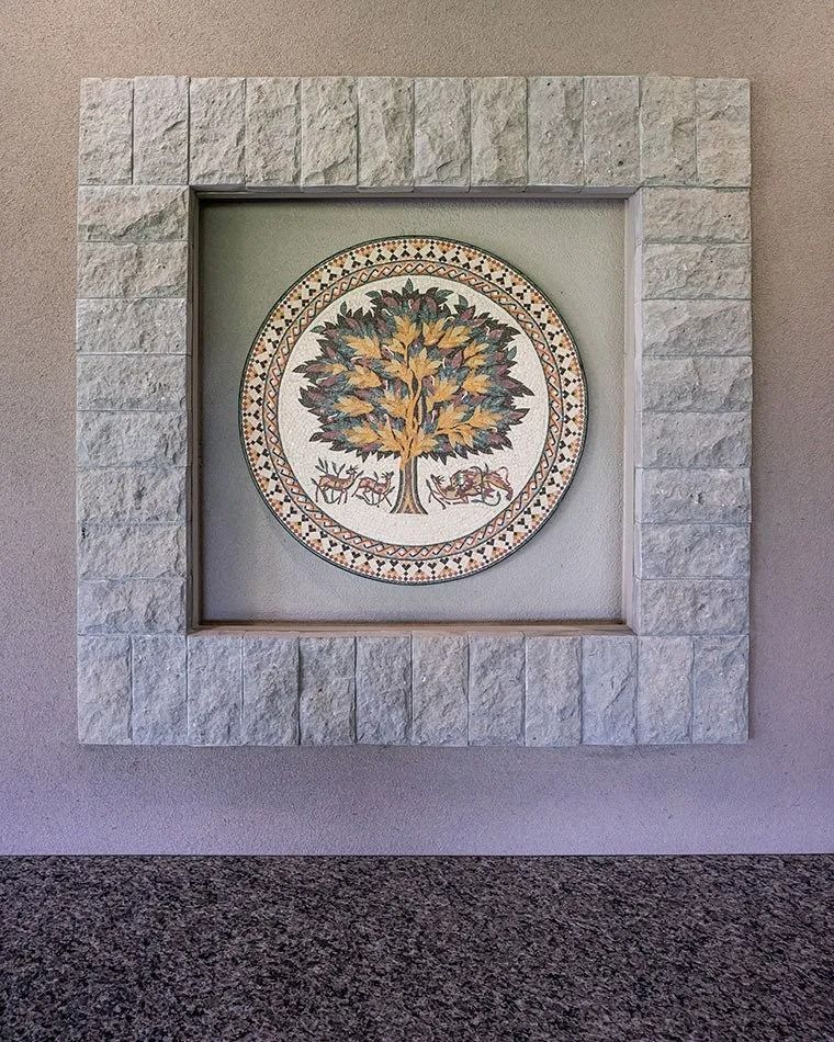 Circular tree mosaic within a stone square frame on a wall.