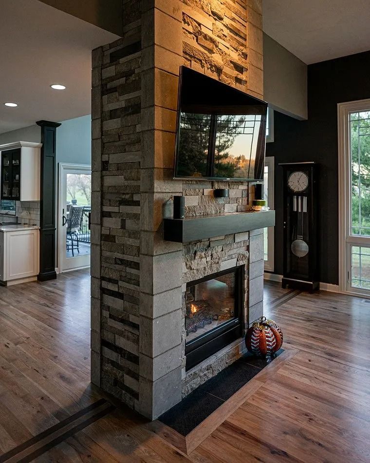 Stone fireplace with TV mounted above, in a room with hardwood floors and a grandfather clock.