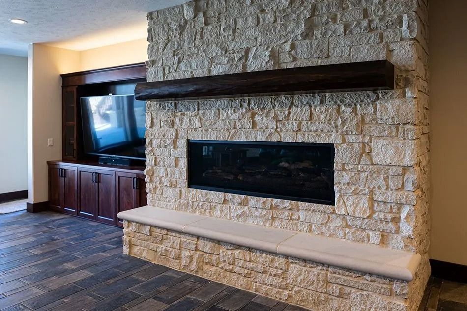 Fireplace with stone facade, dark wood mantel, built-in bench, and television in a living space.