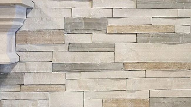 Textured wall of beige, gray, and tan rectangular stone tiles. A white architectural detail is on the left.