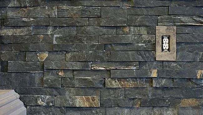 Dark gray stacked stone wall with an electrical outlet.