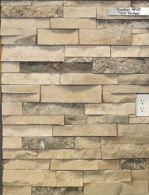 Stone veneer wall sample with Timber Wolf Thin Ledge text, neutral tones, and a power outlet.