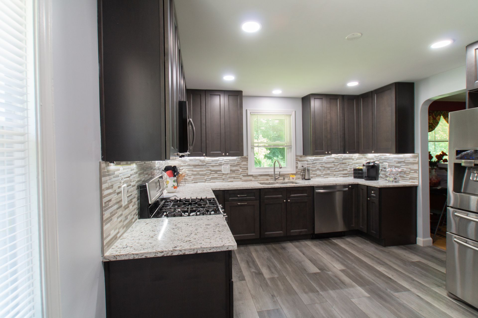 Modern kitchen with dark brown cabinets, light countertops, and gray wood-look flooring.