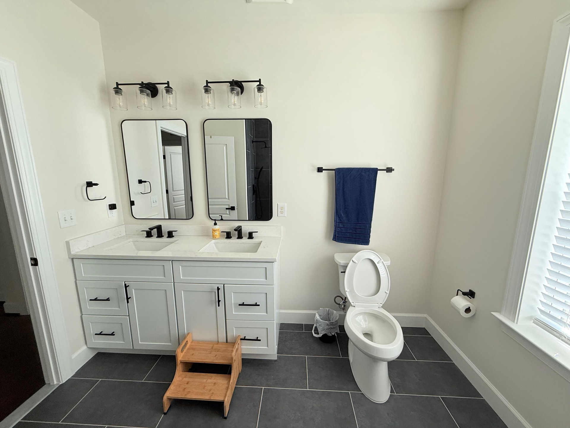 Modern bathroom with dual sinks, wooden-framed mirrors, white countertop, and floating shelves.