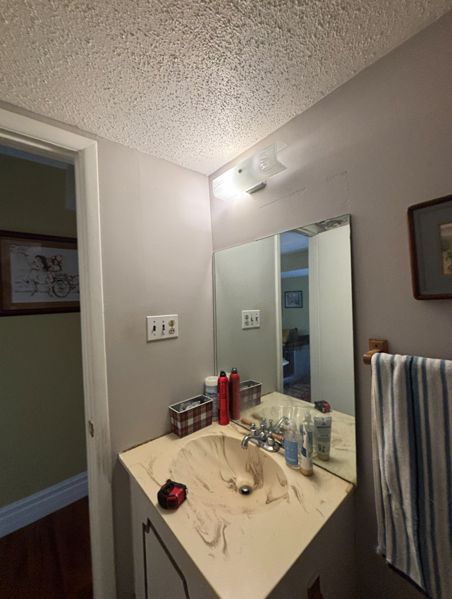A small bathroom vanity with a beige marble-look sink, square mirror, light fixture, and gray walls.