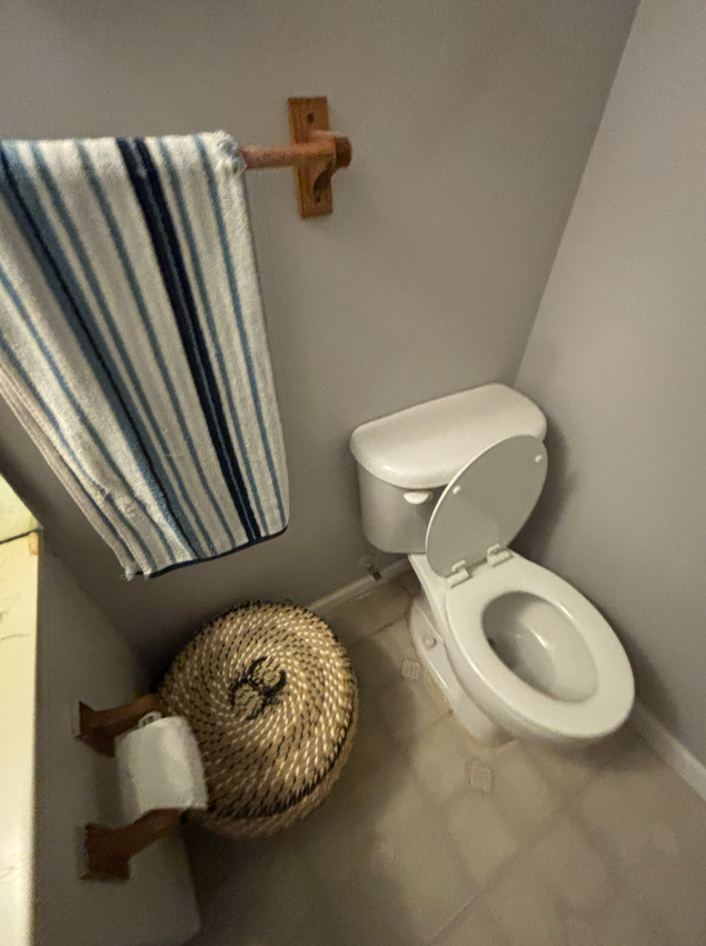 A bathroom corner featuring a white toilet, a woven lidded basket, and a striped towel hanging on a wall-mounted rack.
