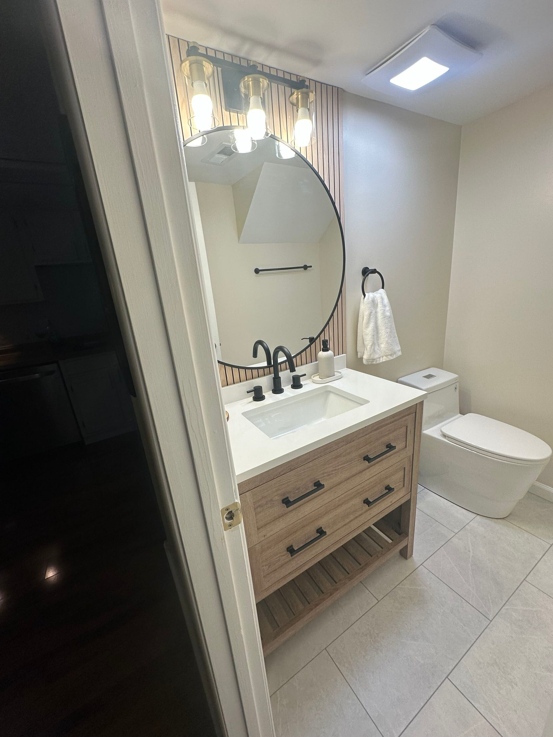Modern bathroom with dual sinks, wooden-framed mirrors, white countertop, and floating shelves.