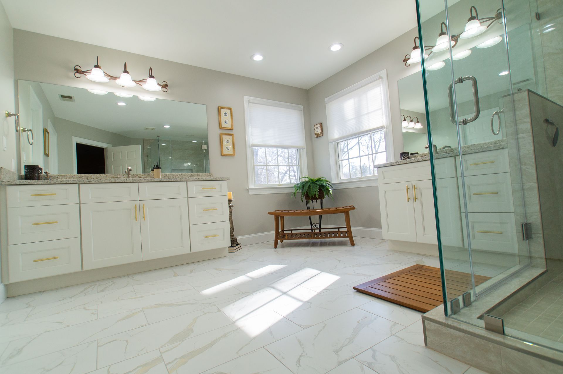 Bright bathroom with white cabinets, large mirrors, and glass shower.