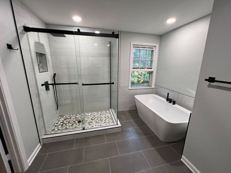 Modern bathroom with gray tiles, a glass shower, a freestanding tub, and a window.