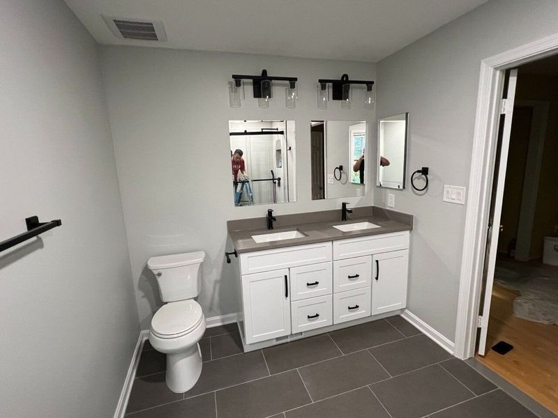 Bathroom with white vanity, gray countertop, dark fixtures, and gray tiled floor.
