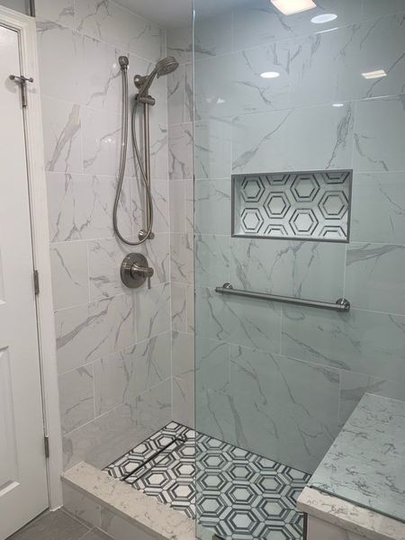 Modern bathroom shower with marble tile, hexagonal floor, glass enclosure, and grab bar.