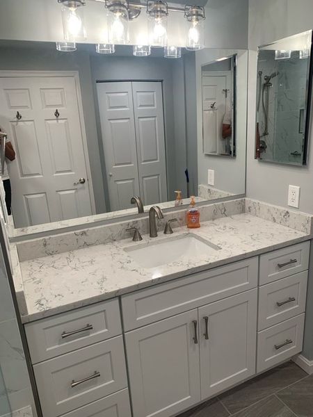 Bathroom vanity with white cabinets, light countertop, large mirror, and overhead lights.