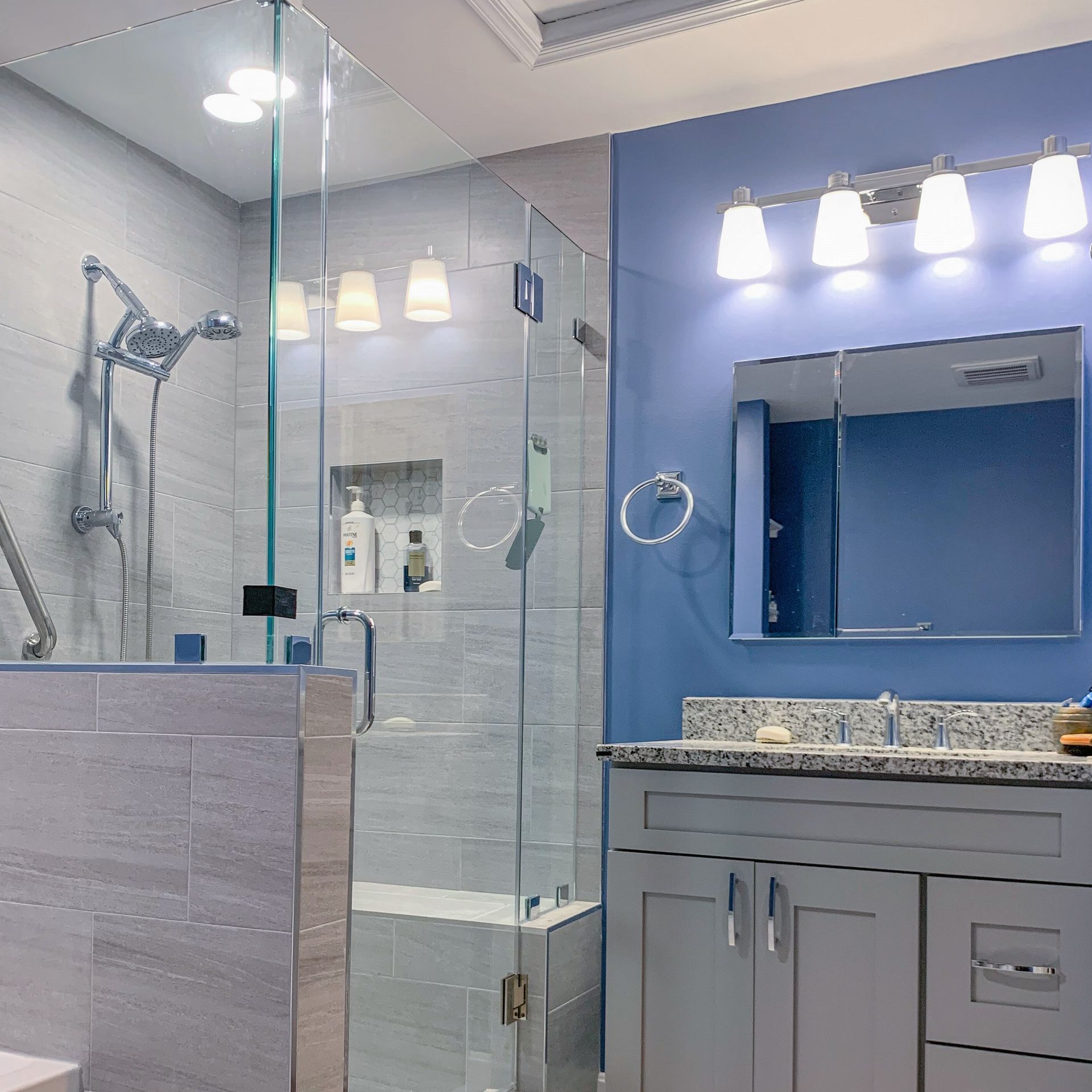 Modern bathroom with a glass shower, blue walls, gray vanity, and bright lights.