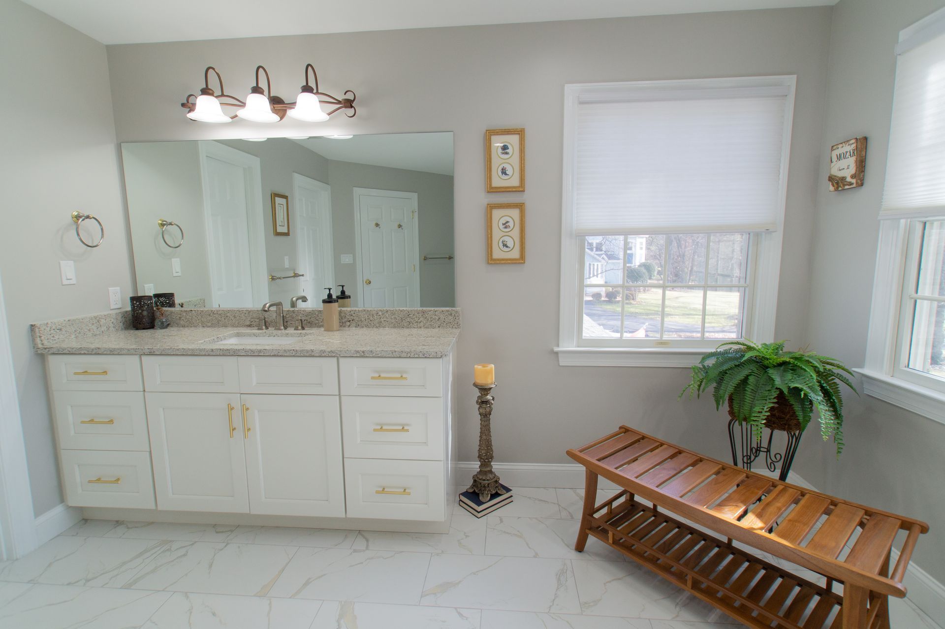 Bathroom with white cabinets, beige countertop, large mirror, white tile floor, and a wooden bench.