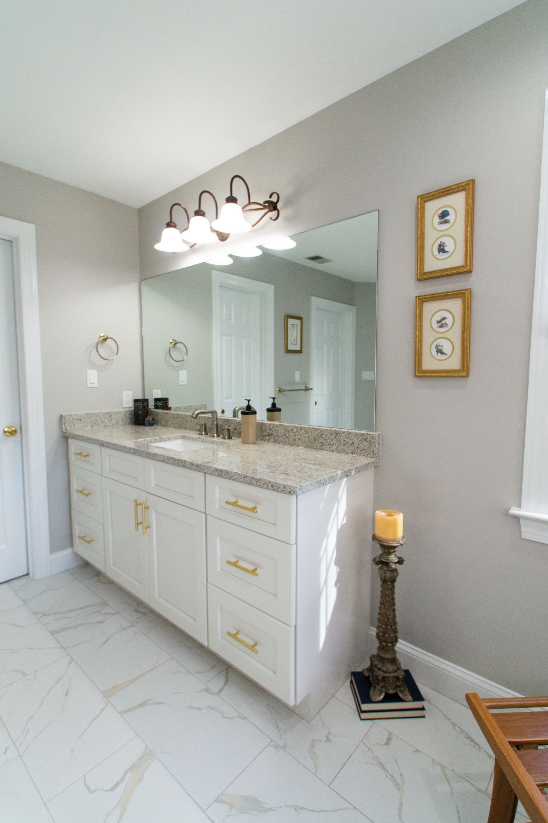 Bathroom with white vanity, gold hardware, granite countertop, large mirror, and decorative wall art.
