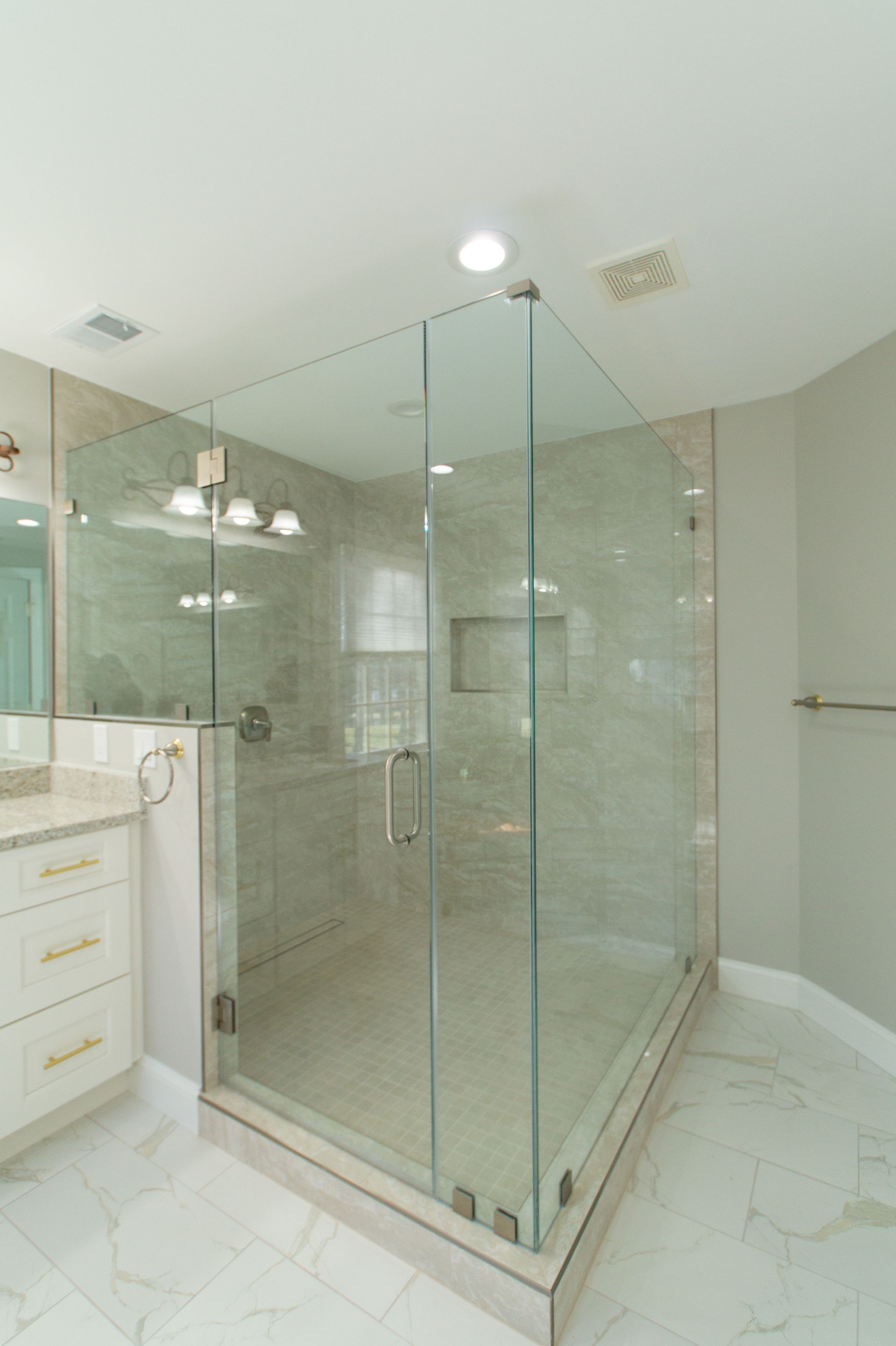 Glass-enclosed shower with tiled walls and floor, corner design in a light-colored bathroom.