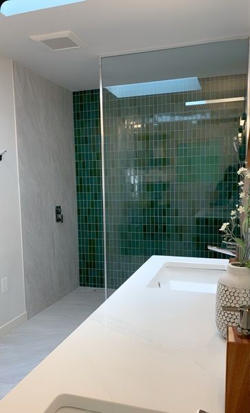 Modern bathroom with white countertops, green tiled shower, and a skylight.