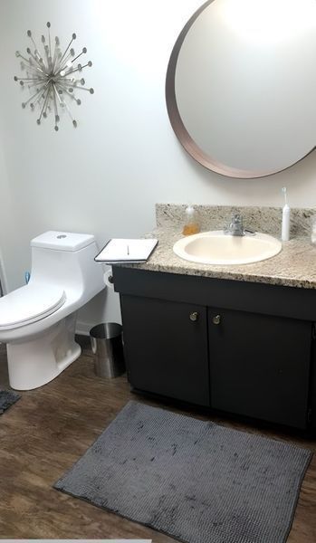 Bathroom with a white toilet, black vanity with a gray countertop, and a large circular mirror.