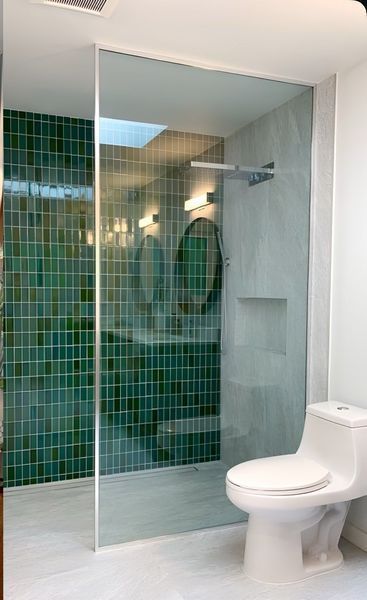 Modern bathroom with green tiled shower, glass panel, toilet, and white walls.
