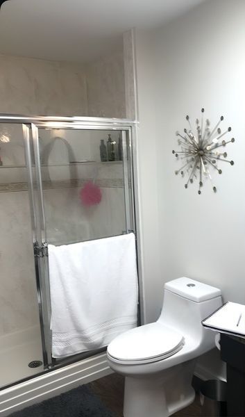 Bathroom with a shower, toilet, and decorative wall art. White walls, chrome fixtures, and a white towel.