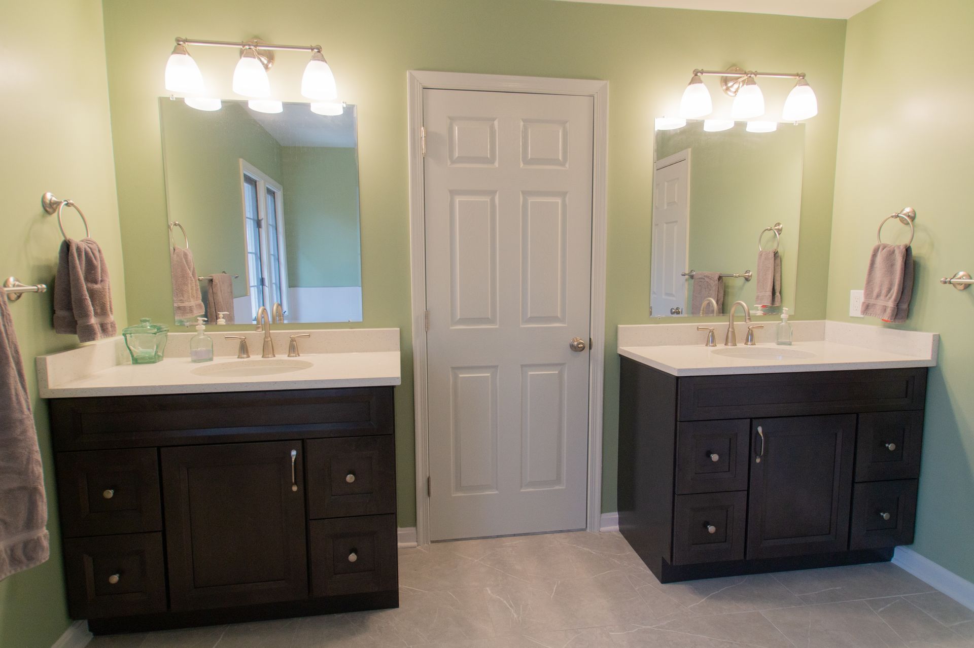 Bathroom with two dark vanities, light green walls, and a white door.