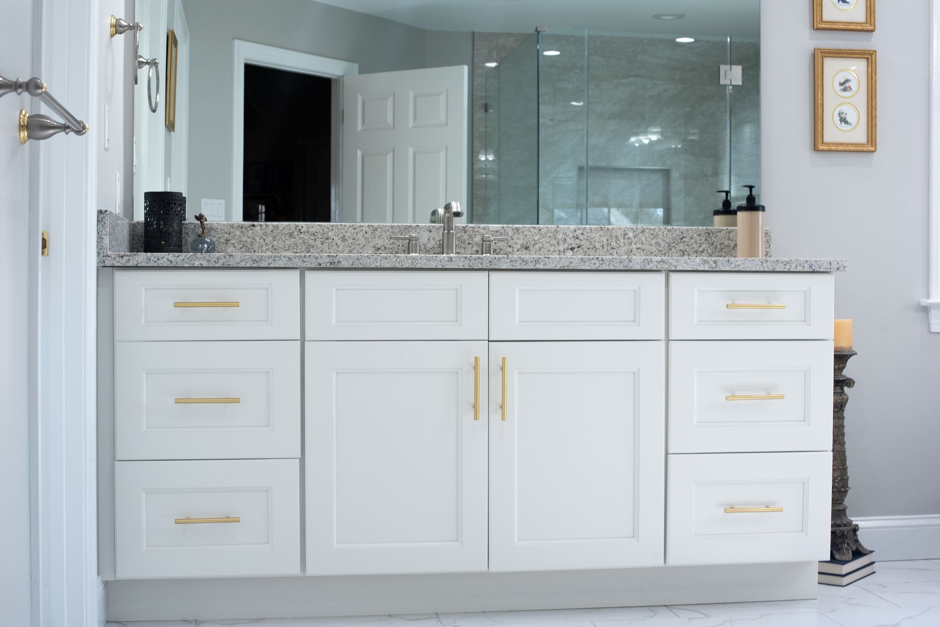 White bathroom vanity with gold hardware, granite countertop, and large mirror.